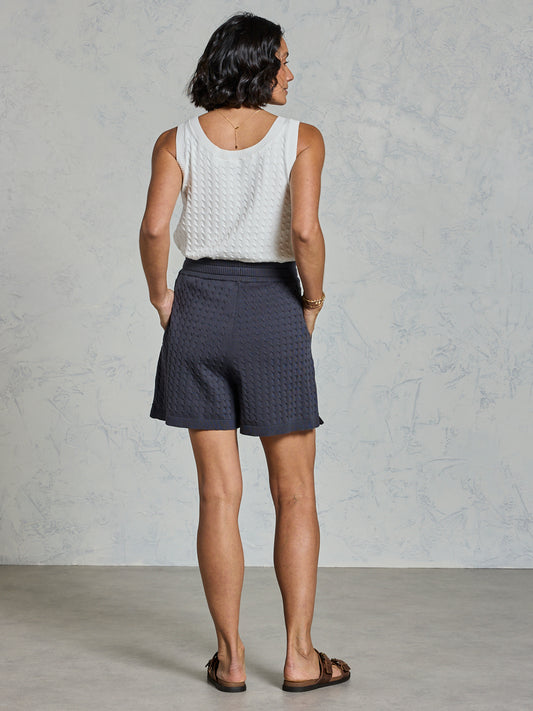 Person wearing a white sleeveless top and dark shorts against a plain background