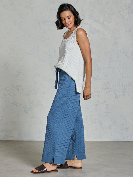 Woman wearing a white sleeveless top and blue patterned pants against a gray background