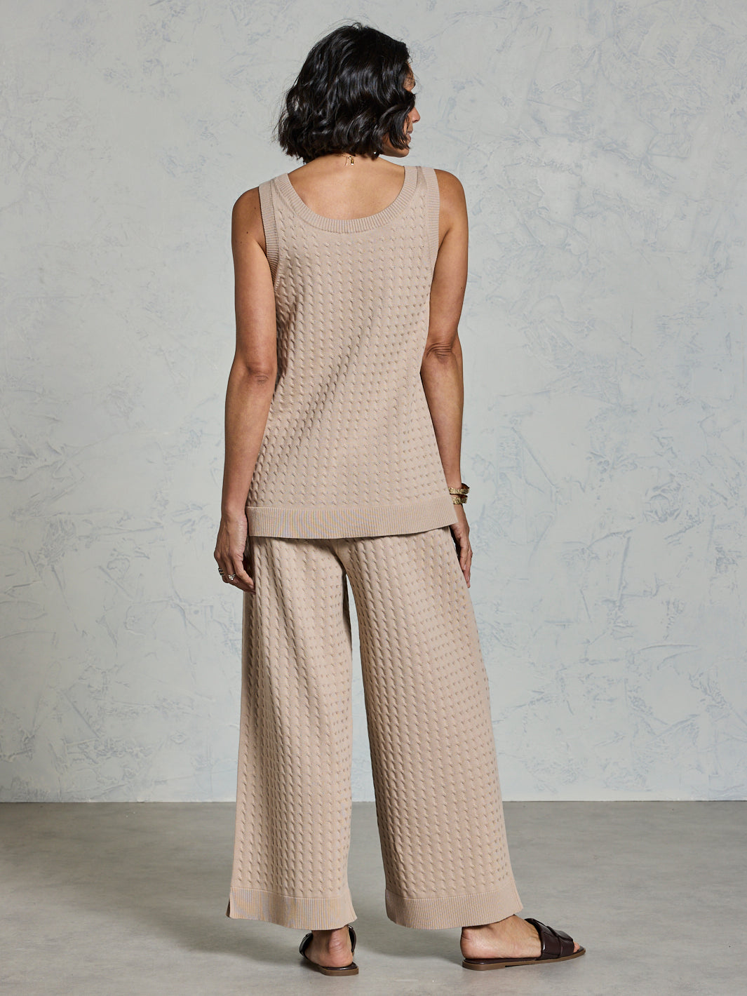 Woman wearing a beige sleeveless top and wide-leg pants against a light gray background