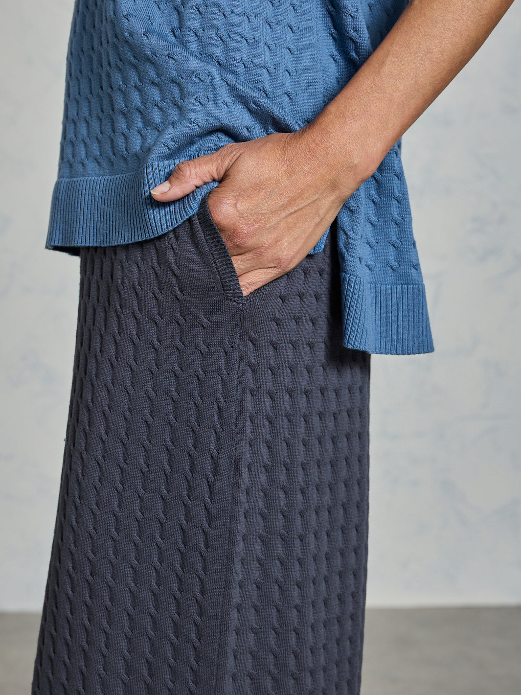 Person wearing a blue textured sweater and gray pants against a neutral background