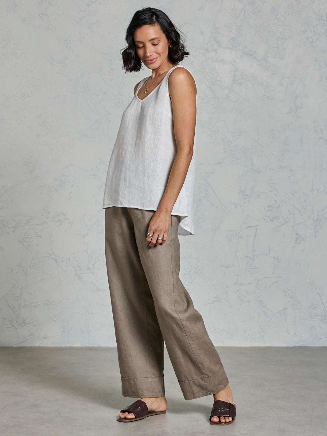 Woman wearing a white sleeveless top and brown wide-leg pants against a gray background