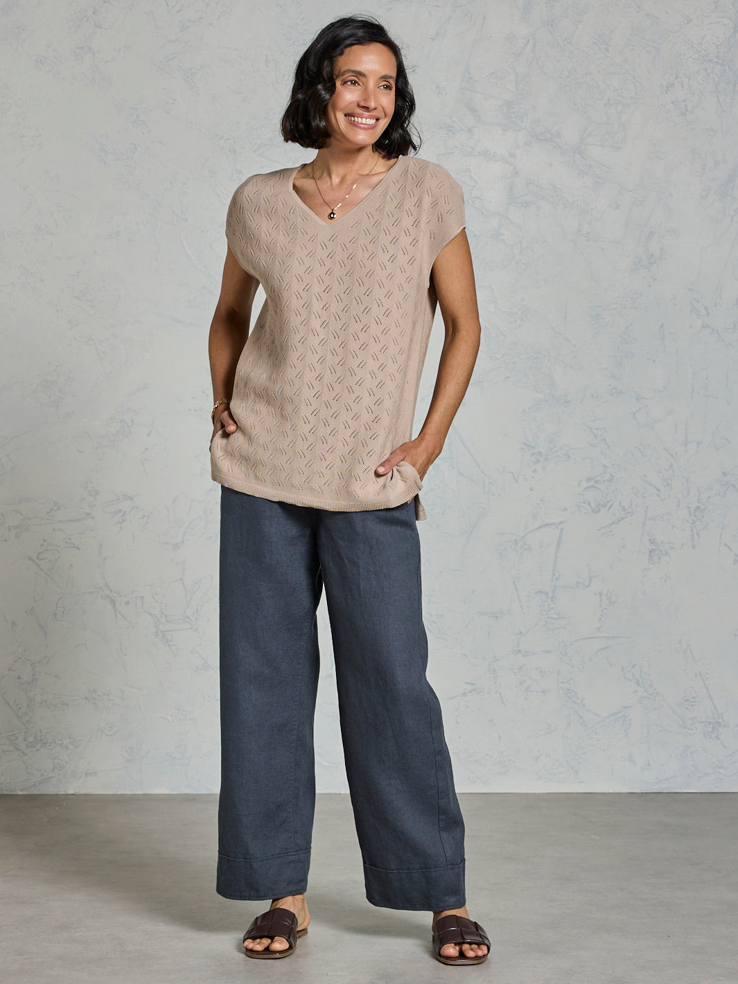 Woman wearing a beige top and dark pants against a plain background