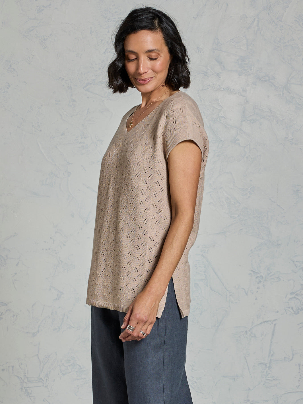 Woman wearing a beige knitted top against a light gray background