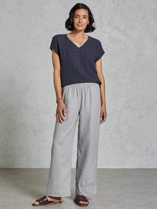 Woman wearing a dark top and light gray pants against a plain background