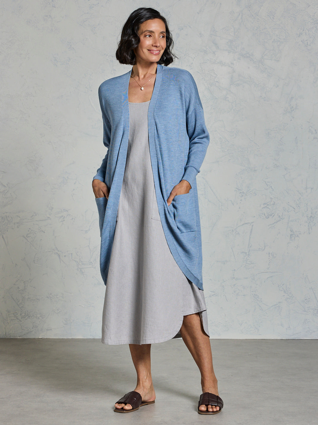 Woman wearing a light blue cardigan over a gray dress against a plain background
