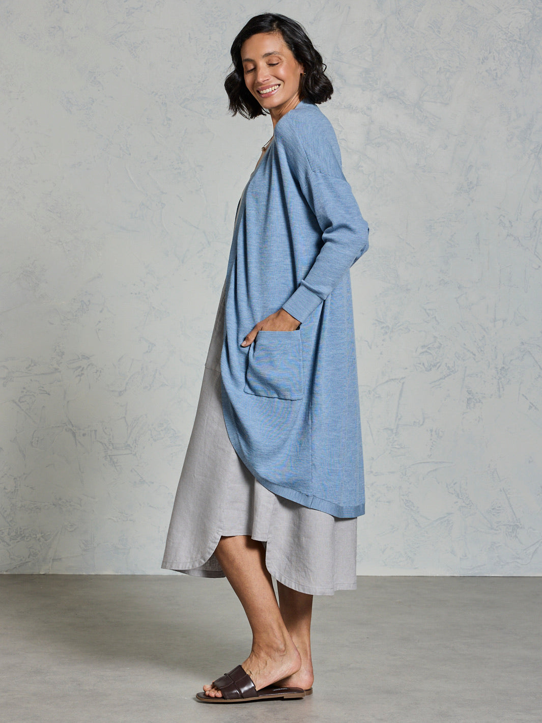 Woman wearing a blue cardigan over a gray dress against a plain background