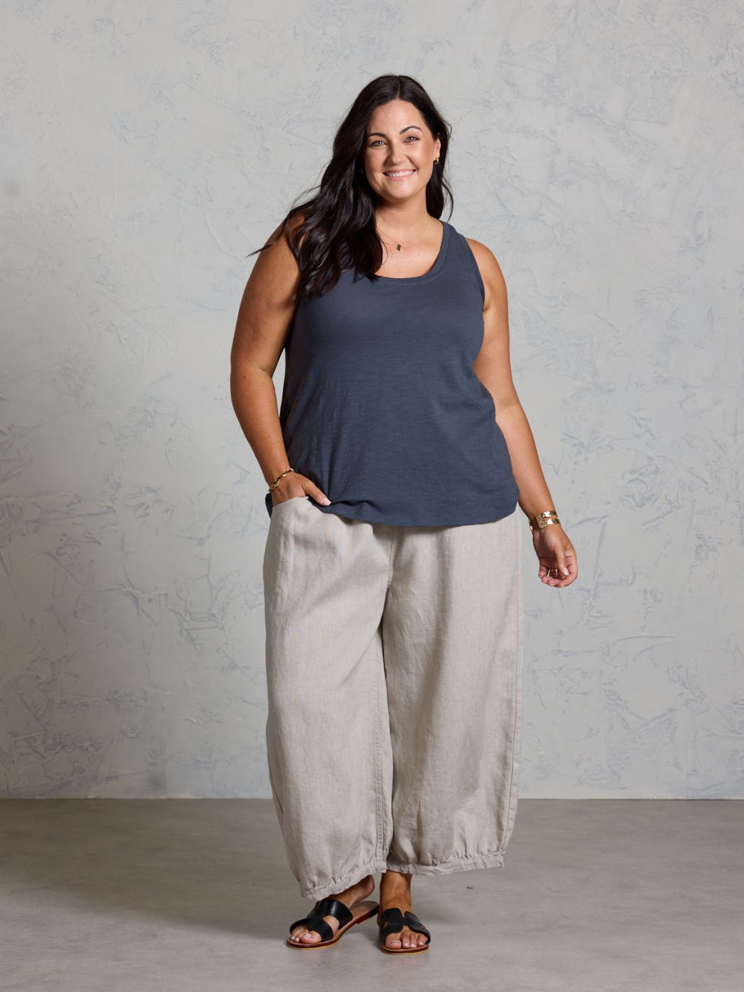 Woman wearing a navy tank top and light gray pants against a plain background