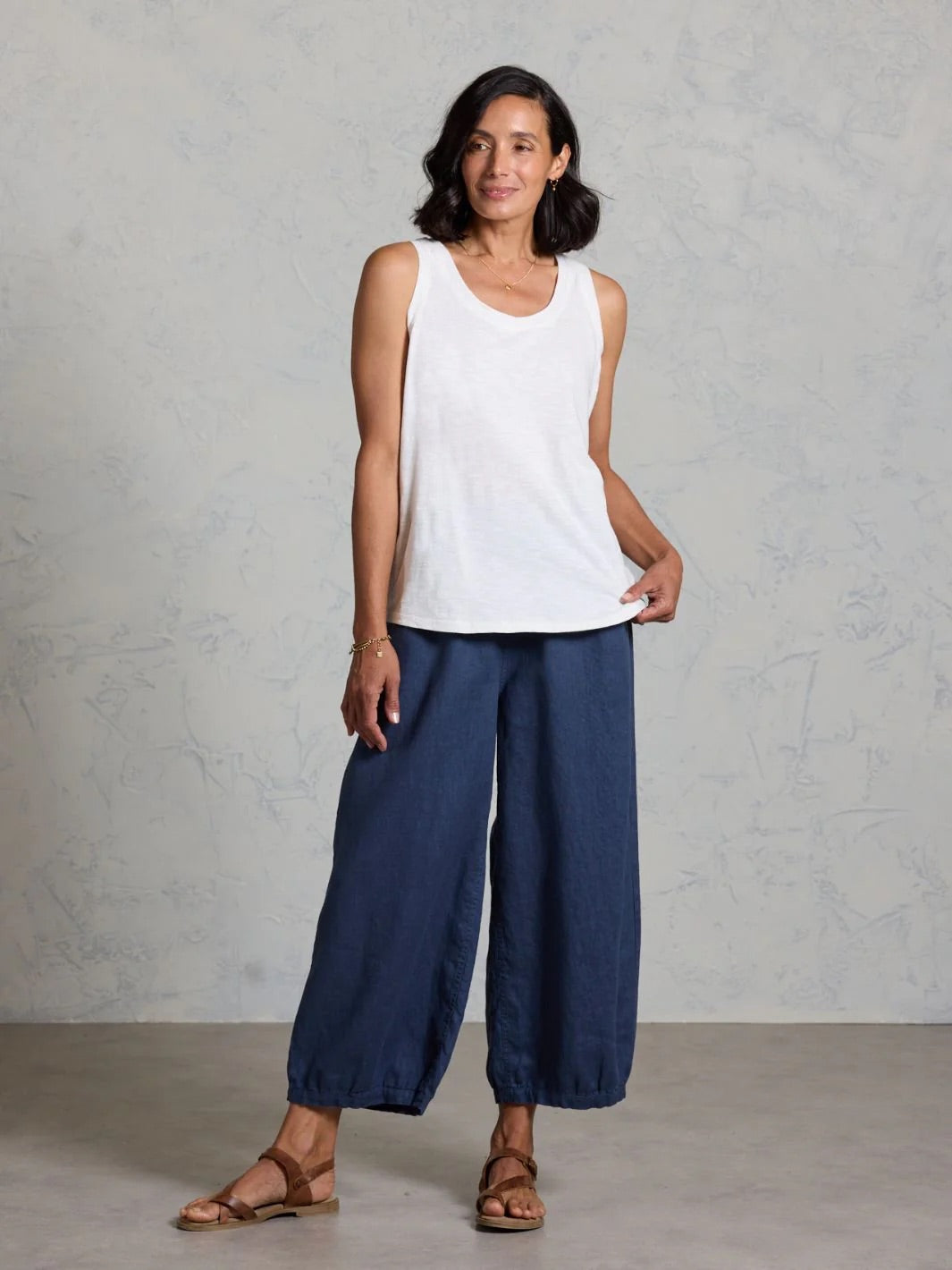 Woman wearing a white sleeveless top and blue pants against a gray background