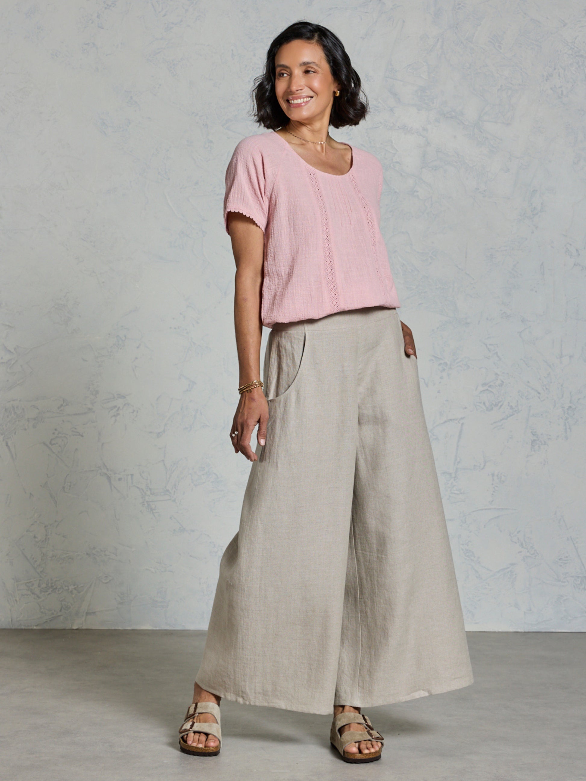 Woman wearing a pink top and beige wide-leg pants against a plain background