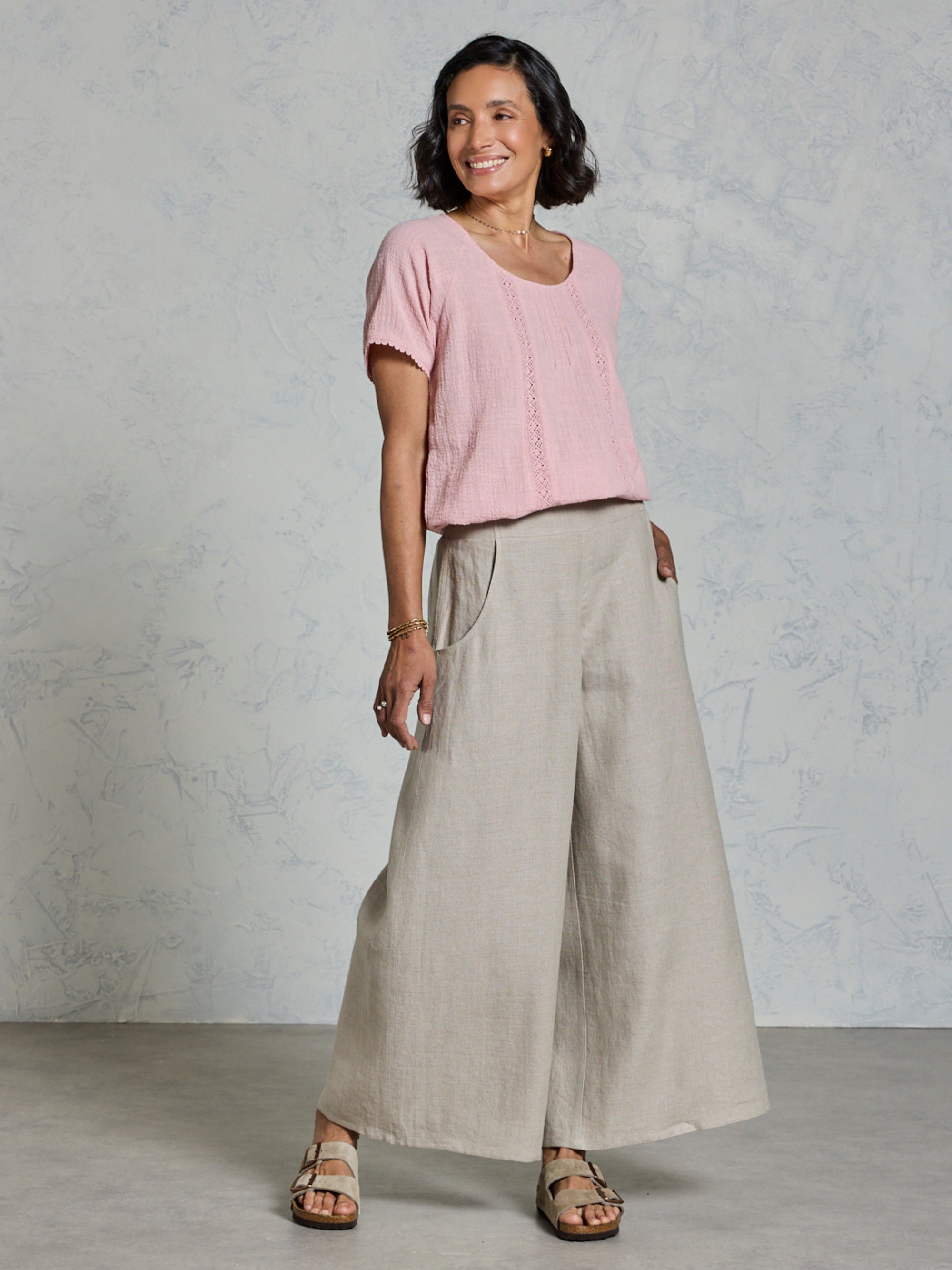 Woman wearing a pink top and beige wide-leg pants against a plain background